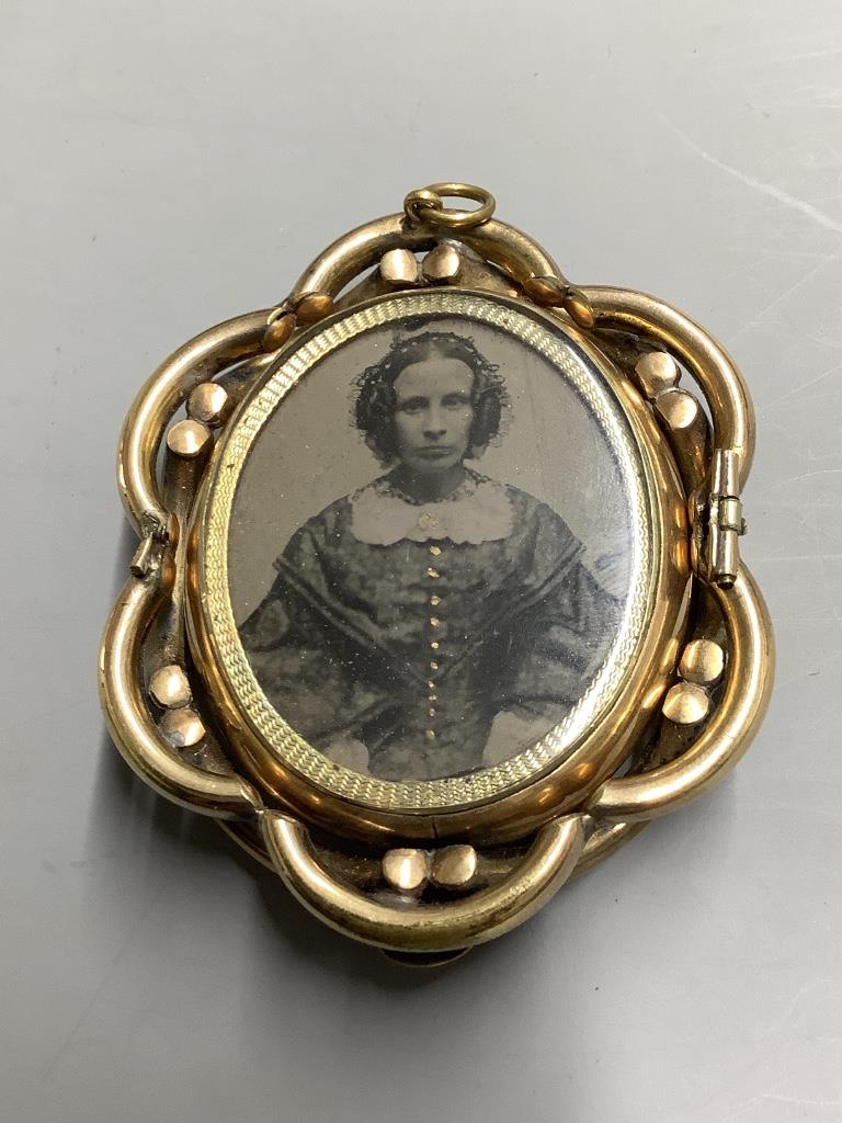 A Victorian pinchbeck and enamel revolving oval mourning pendant brooch, with plaited hair below a glazed panel, 64mm.